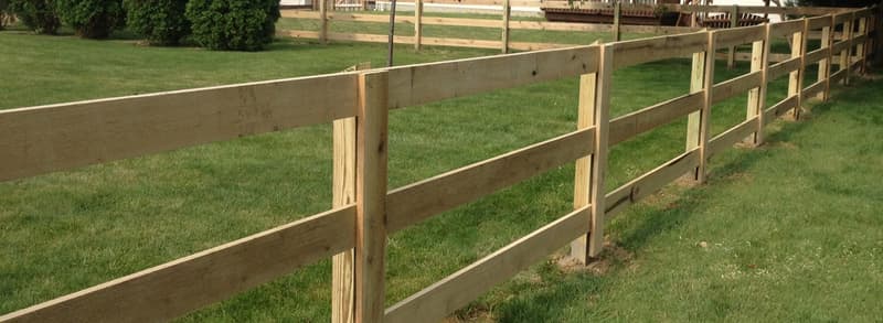 Three-rail wood fence across a green lawn